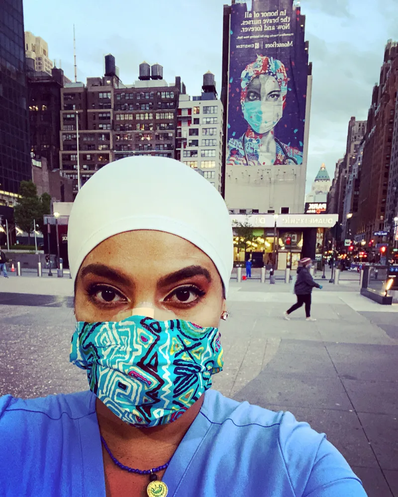 Joanna in a scrub cap and mask, with a mural honouring nurses on the building behind her