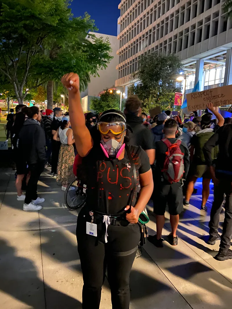 Joanna in a respirator and goggles at an evening march, fist raised